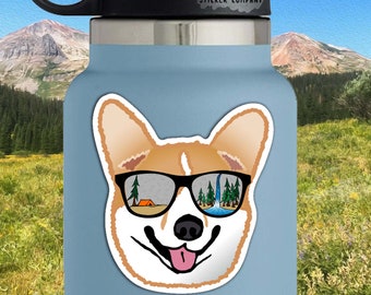 May include: A sticker of a corgi wearing sunglasses with a camping scene reflected in the lenses. The sticker is on a blue water bottle with the text "Life Outside Sticker Company". The sticker is 2.5 inches by 2.5 inches.