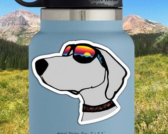 May include: A white dog wearing sunglasses with a sunset and ocean scene. The dog is wearing a colorful patterned collar. The sticker is 3 inches by 2.5 inches.