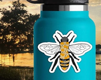 May include: A black and white bee sticker with a yellow and brown honeycomb pattern on its body. The bee has the words "Bee Queen" written on its abdomen. The sticker is on a blue water bottle. The sticker is 3.5 inches by 3 inches.