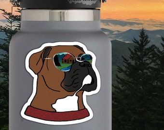 May include: A brown and white boxer dog wearing sunglasses with a reflection of a cabin in the woods. The dog is wearing a red bandana. The sticker is 2.25 inches by 2.75 inches. "Life Outside Sticker Company" is printed at the top of the sticker.