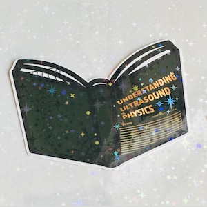 May include: A black and white sticker of an open book with a glittery, holographic finish. The book's title is "Understanding Ultrasound Physics".