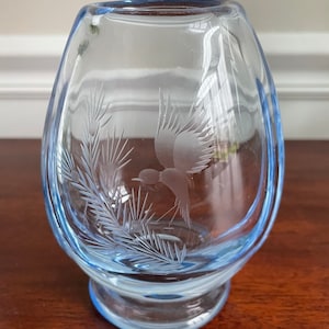 May include: A light blue glass vase with an etched design of a bird flying over a pine branch.
