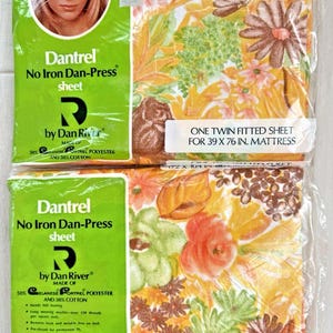 May include: Two packages of Dantrel No Iron Dan-Press sheets. The sheets are in plastic packaging with a floral pattern in shades of yellow, orange, and brown. The packaging includes text and a picture of a woman.