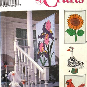 May include: Simplicity Crafts pattern featuring a floral banner with pink and purple irises, a sunflower, a goose in a Dalmatian-patterned cape, and a cardinal with a "Welcome" sign. Also includes goose figurines in wedding attire.