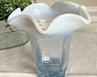 Puede incluir: Un jarrón de vidrio azul y blanco con un borde ondulado. El jarrón está hecho de vidrio opalescente y tiene una base azul clara.