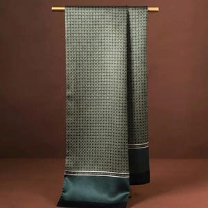 May include: A dark green silk scarf with a repeating circular pattern. The scarf is draped over a gold-coloured rod. The bottom of the scarf has a solid dark green border with a thin white stripe.