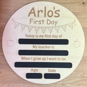 Pu&ograve; includere: Un cartello rotondo in legno con il testo "Arlo's First Day" e uno striscione di bandierine con i pois. Il cartello ha spazi vuoti per scrivere nel testo "Today is my first day of", "My teacher is", "When I grow up I want to be", "Age", e "Date".