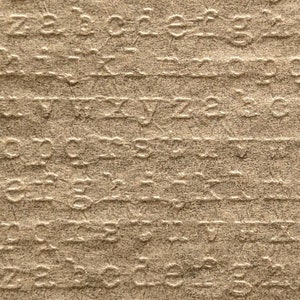 May include: A square, tan paper with embossed lowercase letters. A ruler with inch measurements is at the bottom. The paper is approximately 4 inches wide.