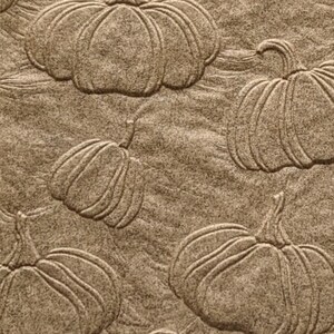 May include: A brown paper napkin with a repeating pattern of embossed pumpkins. The pumpkins are in various sizes and orientations.