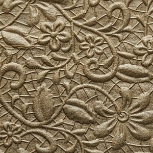 May include: A square piece of brown paper with a raised embossed pattern of flowers and vines. The paper is approximately 4 inches wide.