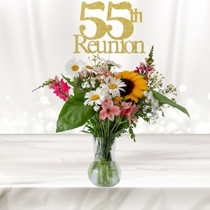 May include: A bouquet of flowers in a clear glass vase with a gold glitter 55th Reunion sign. The flowers include sunflowers, daisies, and pink flowers.