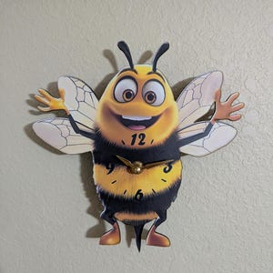 May include: A yellow and black bee-shaped clock with a smiling face and outstretched arms. The clock face has black numbers and gold hands.
