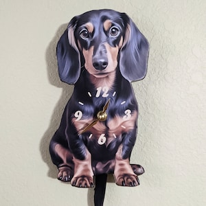 May include: A black and tan dachshund clock with a pendulum tail. The clock face has black numbers and gold hands.