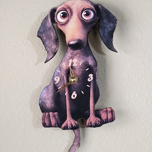 May include: A brown and black dachshund-shaped clock with a white face and black numbers. The clock's hands are gold and the tail is a pendulum.