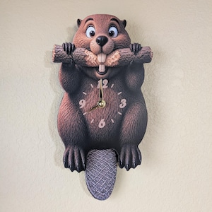 May include: A novelty wall clock shaped like a cartoon beaver, holding a log in its paws. The clock face features a beige background with black numbers and gold hands. The beaver is brown with a gray tail.