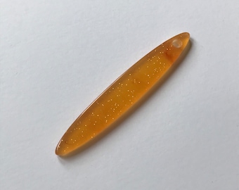 May include: A long, thin, orange-colored pendant with gold glitter embedded in the plastic. The pendant has a small hole at the top for stringing.