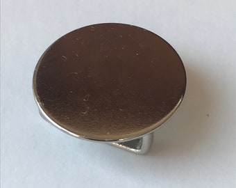 May include: A polished, silver-toned metal button featuring a circular top and a curved, loop-shaped backing. The button has a smooth, reflective surface, and the backing is made of the same material. Suitable for clothing or craft applications.