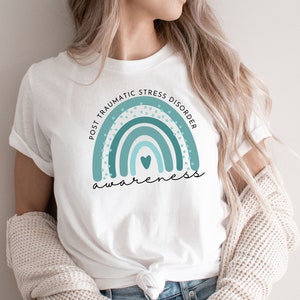 May include: White t-shirt with a teal blue rainbow graphic and the text "Post Traumatic Stress Disorder Awareness".