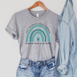May include: Grey t-shirt with a teal rainbow and the text "Post Traumatic Stress Disorder Awareness".