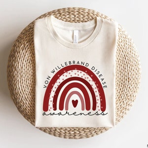 May include: A white t-shirt with a red and pink rainbow design and the text "Von Willebrand Disease Awareness".