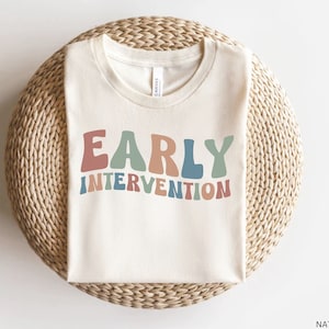 May include: A white t-shirt with the text "EARLY INTERVENTION" in colorful, retro-style lettering.