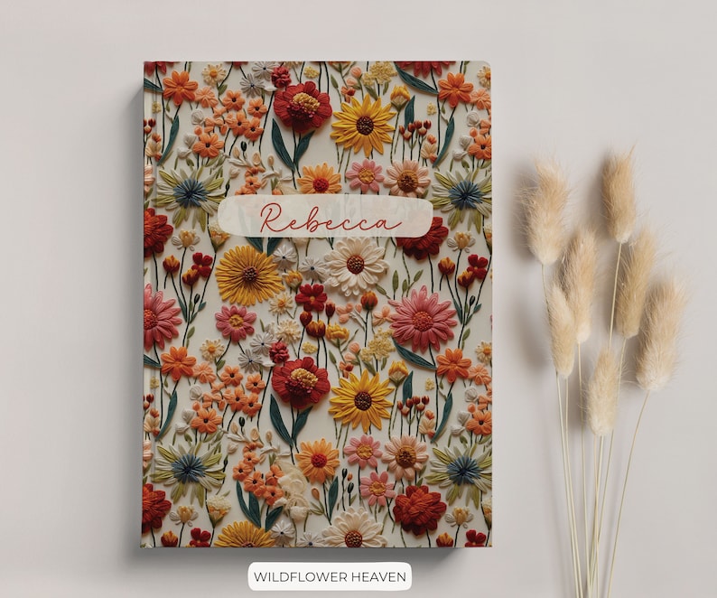 K&ouml;nnte beinhalten: Ein Notizbuch mit floralem Muster und dem Namen "Rebecca" auf dem Einband. Das Notizbuch hat einen wei&szlig;en Hintergrund mit einer Vielzahl von bunten Blumen, darunter rote, orange, gelbe und blaue.