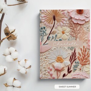 Puede incluir: Un cuaderno personalizado con un dise&ntilde;o floral que presenta una variedad de flores en tonos de rosa, blanco y amarillo. El cuaderno tiene el nombre "Charlotte" impreso en la portada y las palabras "Sweet Summer" impresas debajo de la imagen.