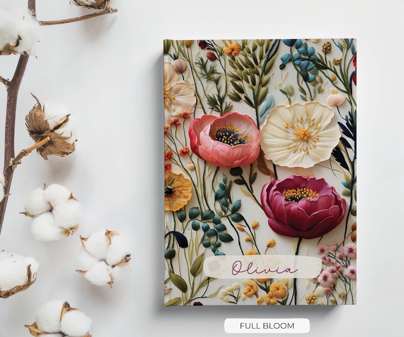 May include: A floral notebook with a white background and a variety of colourful flowers, including pink, red, and yellow. The notebook has a personalised name, "Olivia", and the text "Full Bloom" at the bottom.