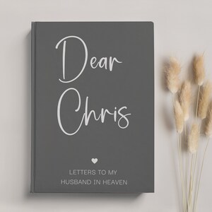 May include: A gray journal with the text "Dear Chris" in white lettering. Below the name, it says "Letters to my Husband in Heaven" with a small heart symbol.