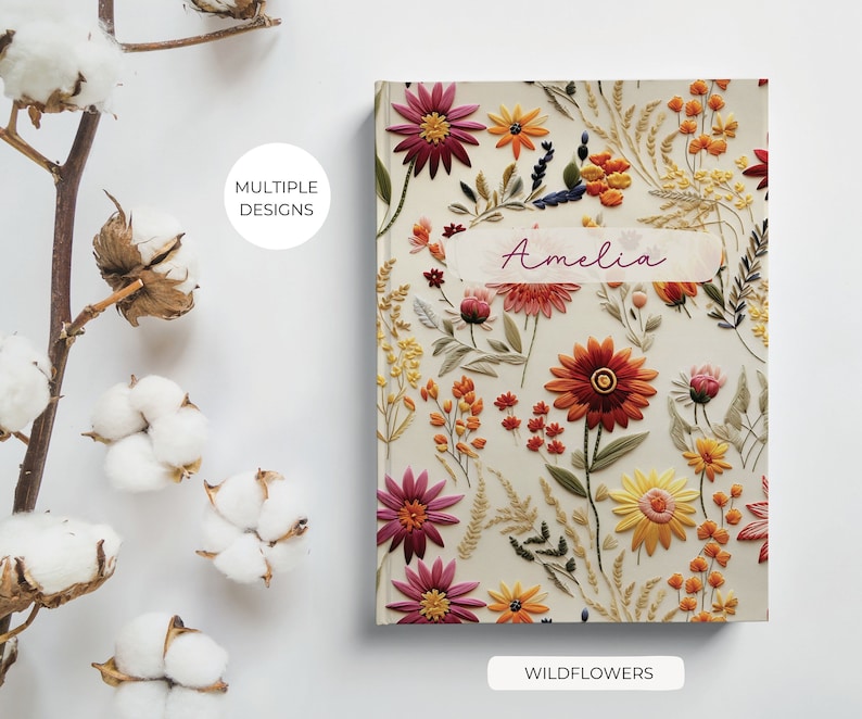 K&ouml;nnte beinhalten: Ein personalisiertes Notizbuch mit einem floralen Design mit gestickten Wildblumen in Rot-, Orange-, Gelb- und Rosat&ouml;nen. Der Notizbuchumschlag tr&auml;gt den Namen "Amelia" und die Worte "Wildflowers" unten.