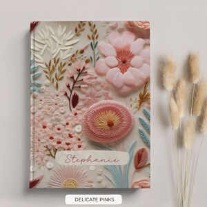 K&ouml;nnte beinhalten: Ein wei&szlig;es Journal mit einem floralen Design mit rosa, roten und blauen Blumen. Das Journal tr&auml;gt den Namen "Stephanie" und die Worte "Delicate Pinks" sind unter dem Bild gedruckt.