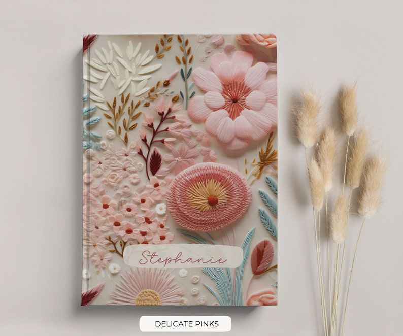 K&ouml;nnte beinhalten: Ein wei&szlig;es Journal mit einem floralen Design mit rosa, roten und blauen Blumen. Das Journal tr&auml;gt den Namen "Stephanie" und die Worte "Delicate Pinks" sind unter dem Bild gedruckt.