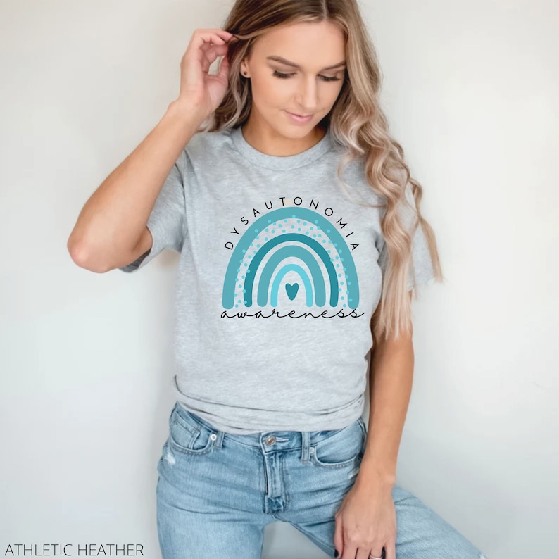 Puede incluir: Una camiseta gris con un dise&ntilde;o de arco&iacute;ris azul y turquesa y el texto "Dysautonomia Awareness" en negro.