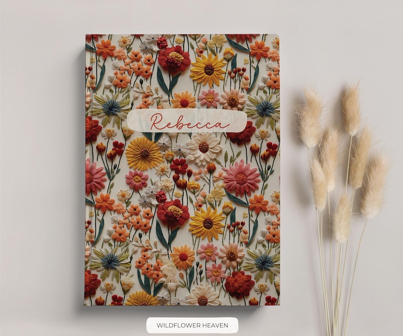 May include: A personalised notebook with a floral design featuring a variety of flowers in shades of red, orange, yellow, and white. The name "Rebecca" is printed on the front cover.