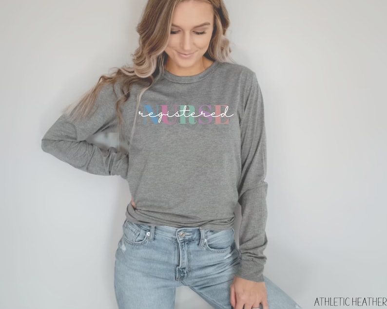 May include: A gray long-sleeve shirt with the text "registered nurse" in colorful letters. The shirt is being worn by a person with long brown hair.