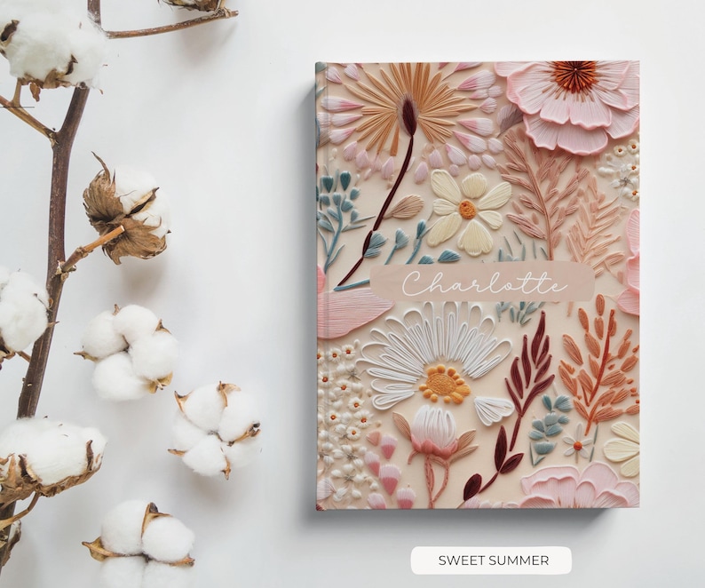 May include: A pink and cream floral notebook with the name "Charlotte" printed on the front cover. The notebook features a floral design with a variety of flowers and leaves. The text "Sweet Summer" is printed below the notebook.