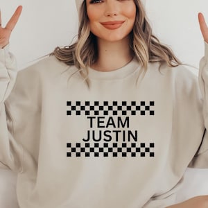 May include: A beige sweatshirt with black checkered trim and the text "TEAM JUSTIN" printed on the front.