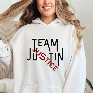 May include: White hoodie with black text that reads "TEAM JUSTICE" with the word "JUSTICE" crossed out in red.