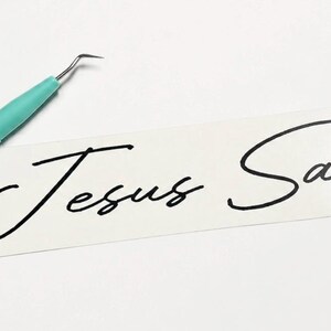 May include: A rectangular white vinyl decal featuring the black cursive text Jesus Saves, accompanied by a mint green weeding tool with a thin metal hook tip, used for removing excess material from the adhesive backing during the application process.