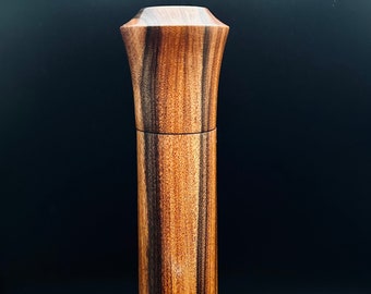 Op de afbeelding: Een hoge, houten pepermolen met een donkerbruin en roodbruin gestreept patroon. De molen heeft een afgeronde bovenkant en een cilindrisch lichaam.