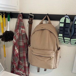 May include: A black metal rack with hooks holding a brown backpack, a plaid shirt, a brown leather belt, a yellow duster, a green duster, and two pairs of black and green sneakers.