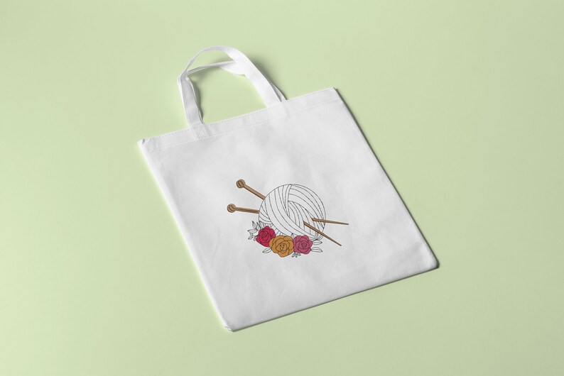 May include: White tote bag with a black and white illustration of a ball of yarn with knitting needles and a floral wreath. The flowers are red, pink, and orange.