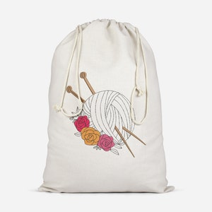 May include: A white drawstring bag with a design of a ball of yarn, knitting needles, and flowers. The flowers are red, orange, and pink.