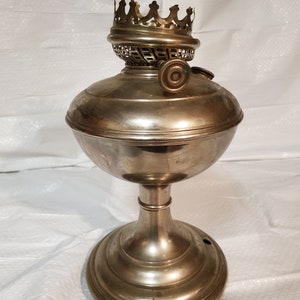 以下が含まれることがあります： 王冠の形をした装飾的なトップと丸いベースを持つ銀色のオイルランプ。ランプには芯とガラスの煙突があります。