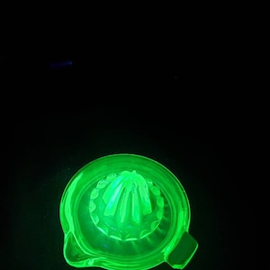 Op de afbeelding: Een groene glazen citruspers met een geribbeld ontwerp. De pers is gemaakt van uraniumglas en gloeit onder zwart licht.