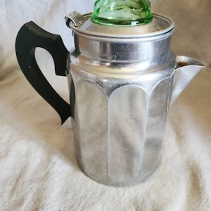 May include: A silver percolator coffee pot with a black handle and a green glass lid.