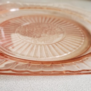 Puede incluir: Un plato vintage de cristal rosa, de forma cuadrada con bordes festoneados. El plato presenta un diseño central con líneas radiales y detalles florales. Ideal para servir aperitivos o postres.