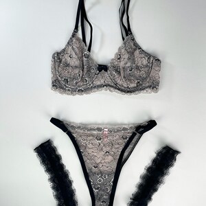 May include: A black and nude lace lingerie set with a bra, panty, and two garters.