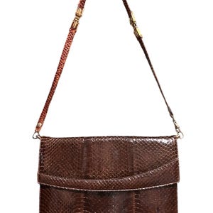 Könnte beinhalten: Eine braune Leder-Umhängetasche mit Klappenverschluss. Die Tasche hat ein strukturiertes Schlangenmuster und einen dünnen, verstellbaren Riemen mit goldfarbenen Beschlägen. Die Tasche ist etwa 30 cm breit und 20 cm hoch.