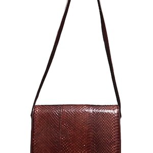 Op de afbeelding: Een bruine schoudertas van slangenleer met een gouden sluiting. De tas heeft een lange schouderband en een klep sluiting.